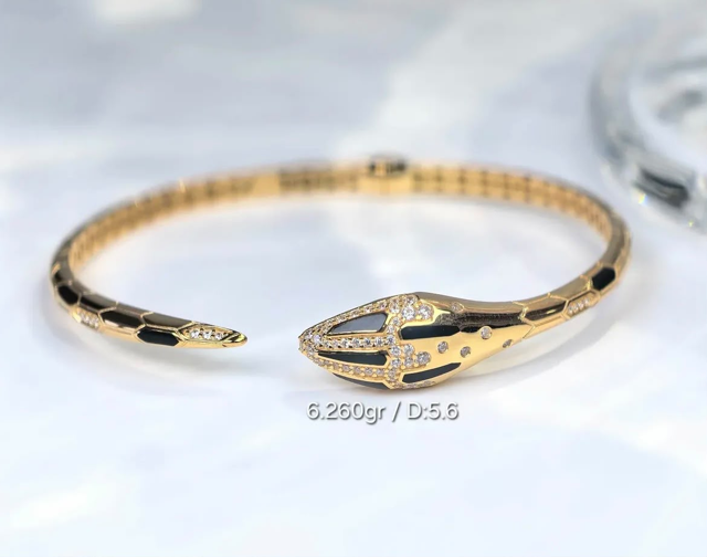Gelang emas kaku terbuka model kepala ular bertabur permata dengan aksen enamel hitam.